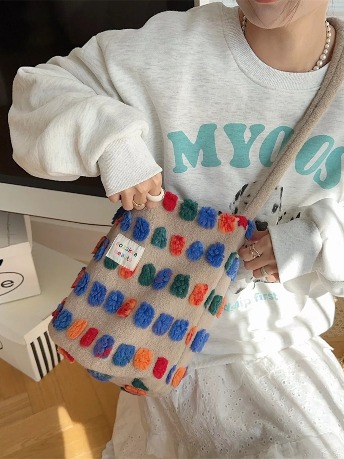 Person wearing a white sweatshirt with teal text, holding a colorful textured bag.
