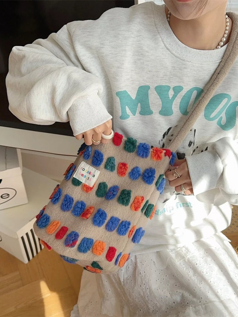Person wearing a white sweatshirt with teal text, holding a colorful textured bag.