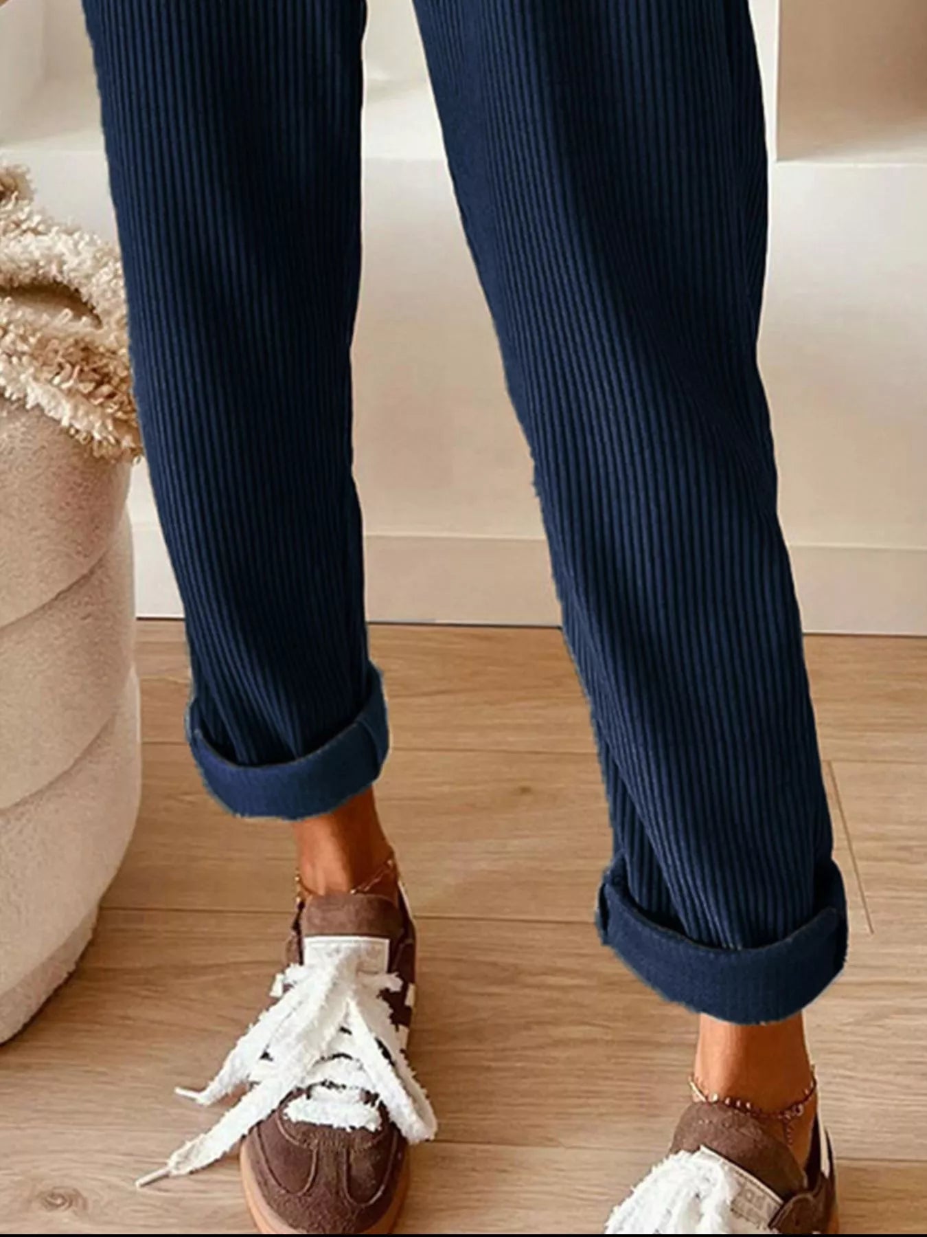 Navy blue ribbed pants with rolled-up cuffs worn with brown loafers on a wooden floor.