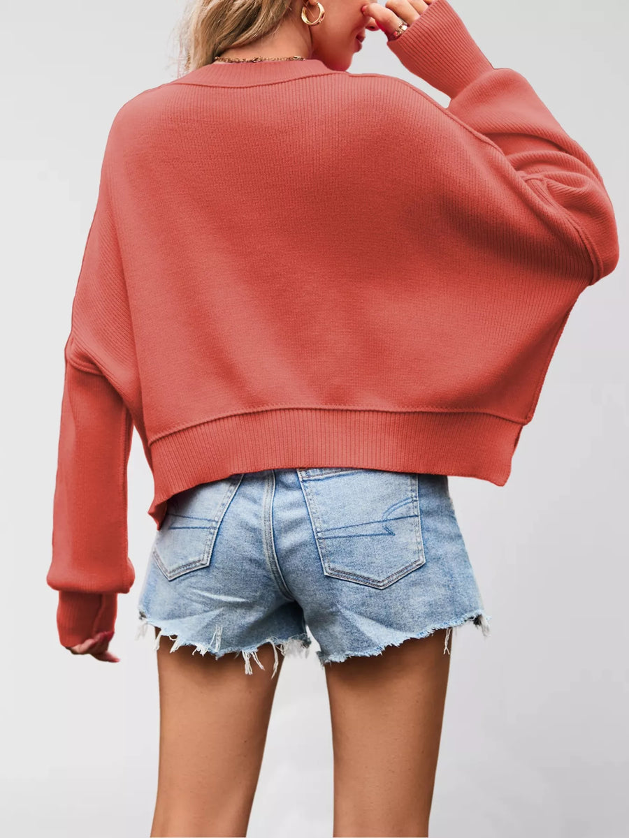Person wearing a red sweater and denim shorts on a plain background
