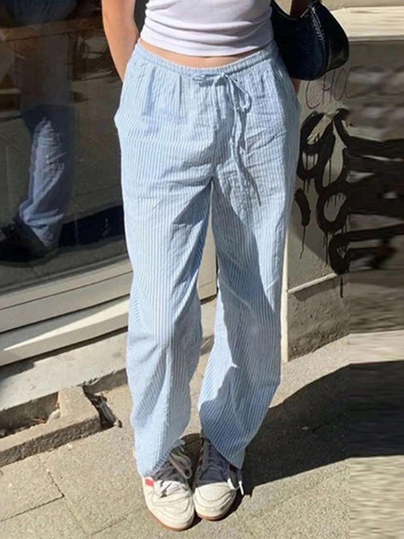 Person wearing light blue checkered pants standing on a sidewalk.