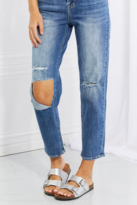 Ripped blue jeans worn by a person on a white background