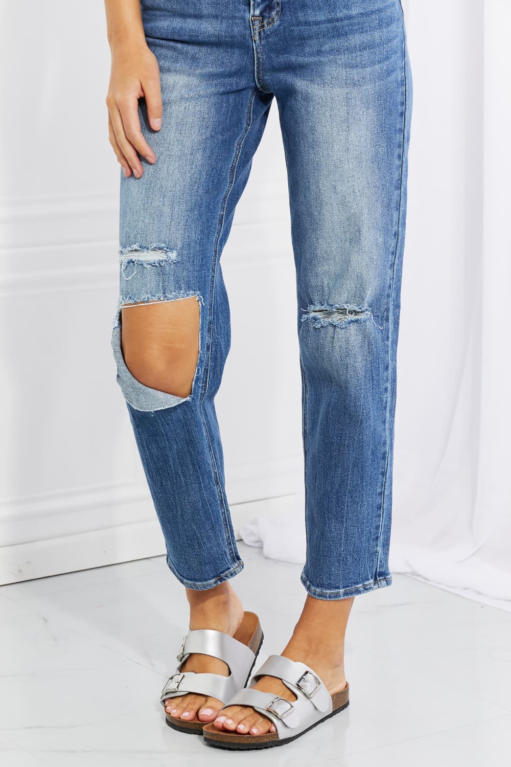 Ripped blue jeans worn by a person on a white background