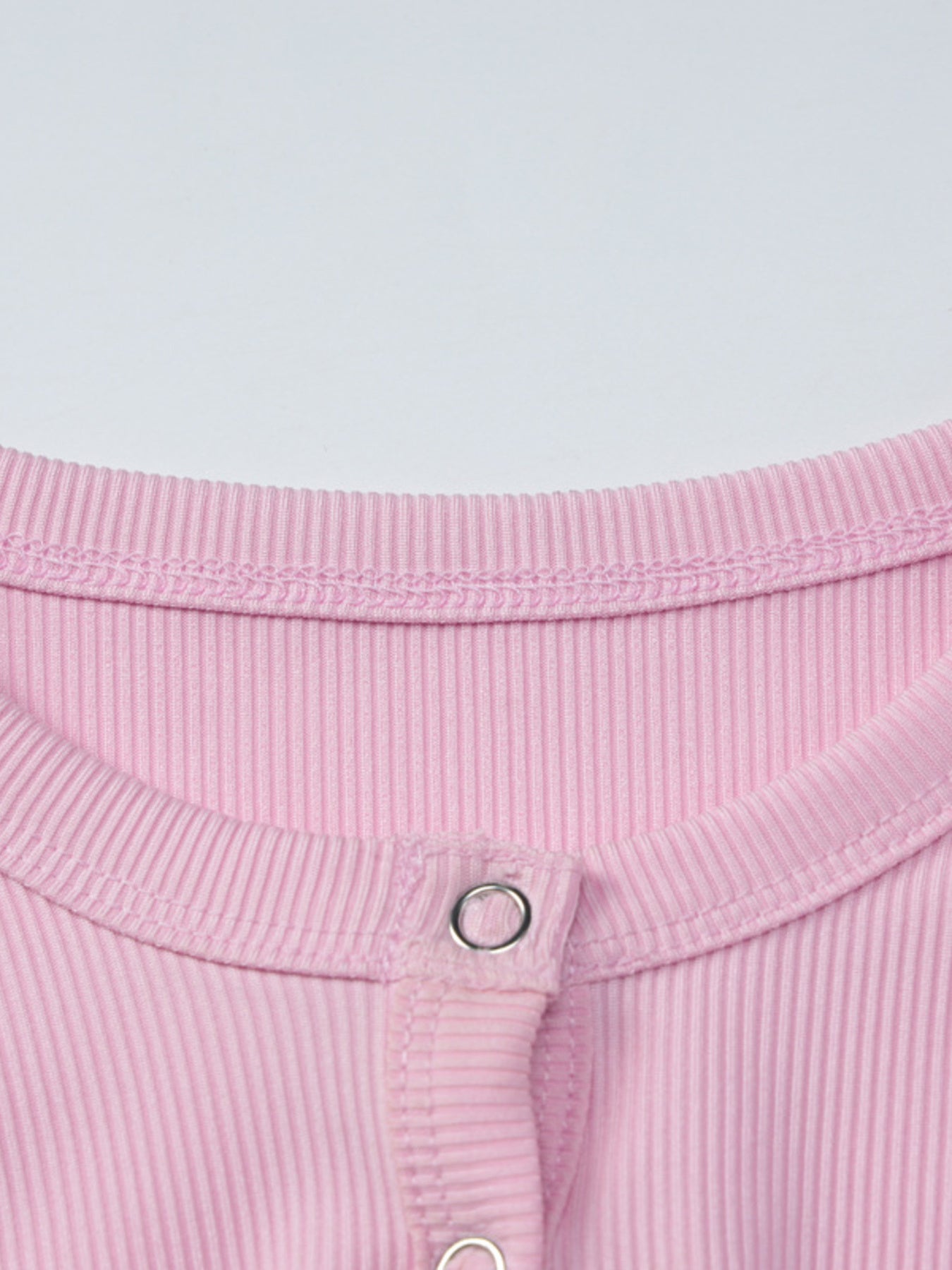Close-up of a pink ribbed fabric with a button on a light gray background