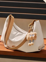 White handbag with a brown strap and a plush keychain on a wooden surface.