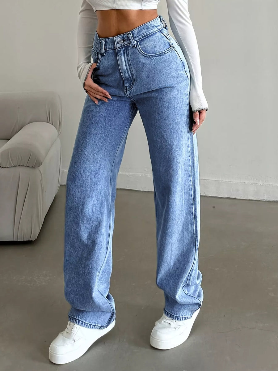 Person wearing blue jeans and white sneakers in a minimal indoor setting