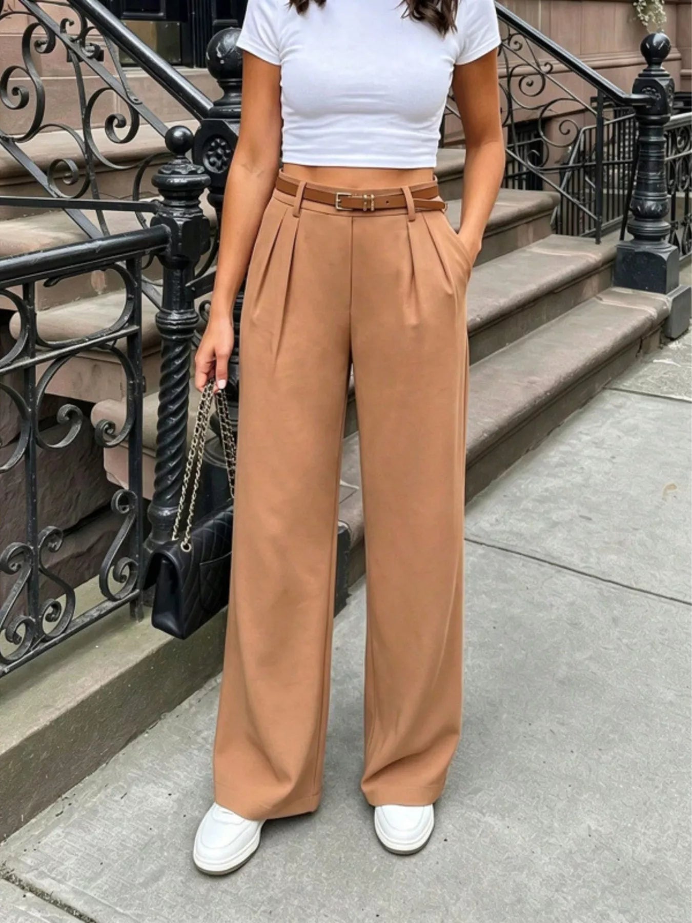 Person wearing a white top and tan wide-leg pants standing on a city street.