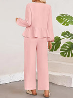 Person wearing a pink outfit with ruffled top and wide-leg pants, standing against a light-colored wall with green leaves.