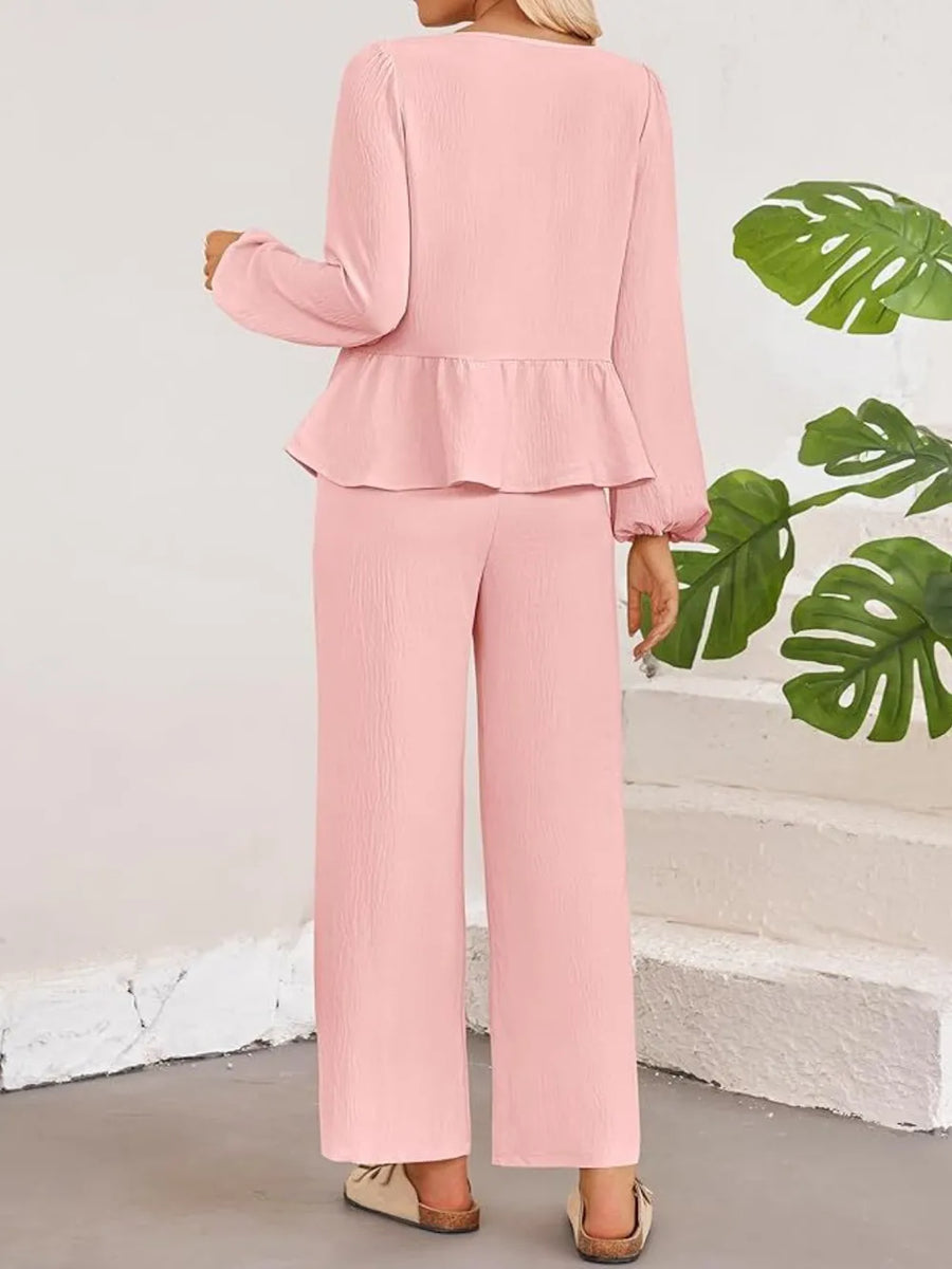 Person wearing a pink outfit with ruffled top and wide-leg pants, standing against a light-colored wall with green leaves.