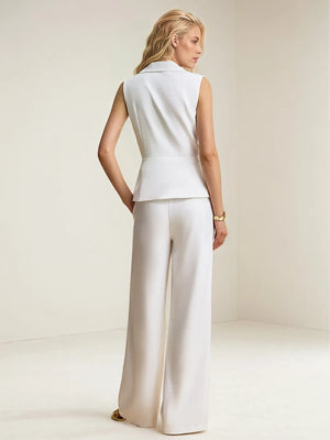 Woman wearing a white sleeveless top and wide-leg pants on a plain background