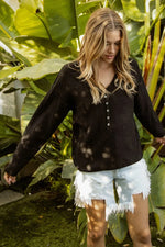 Woman in a black blouse and white shorts standing among large green leaves