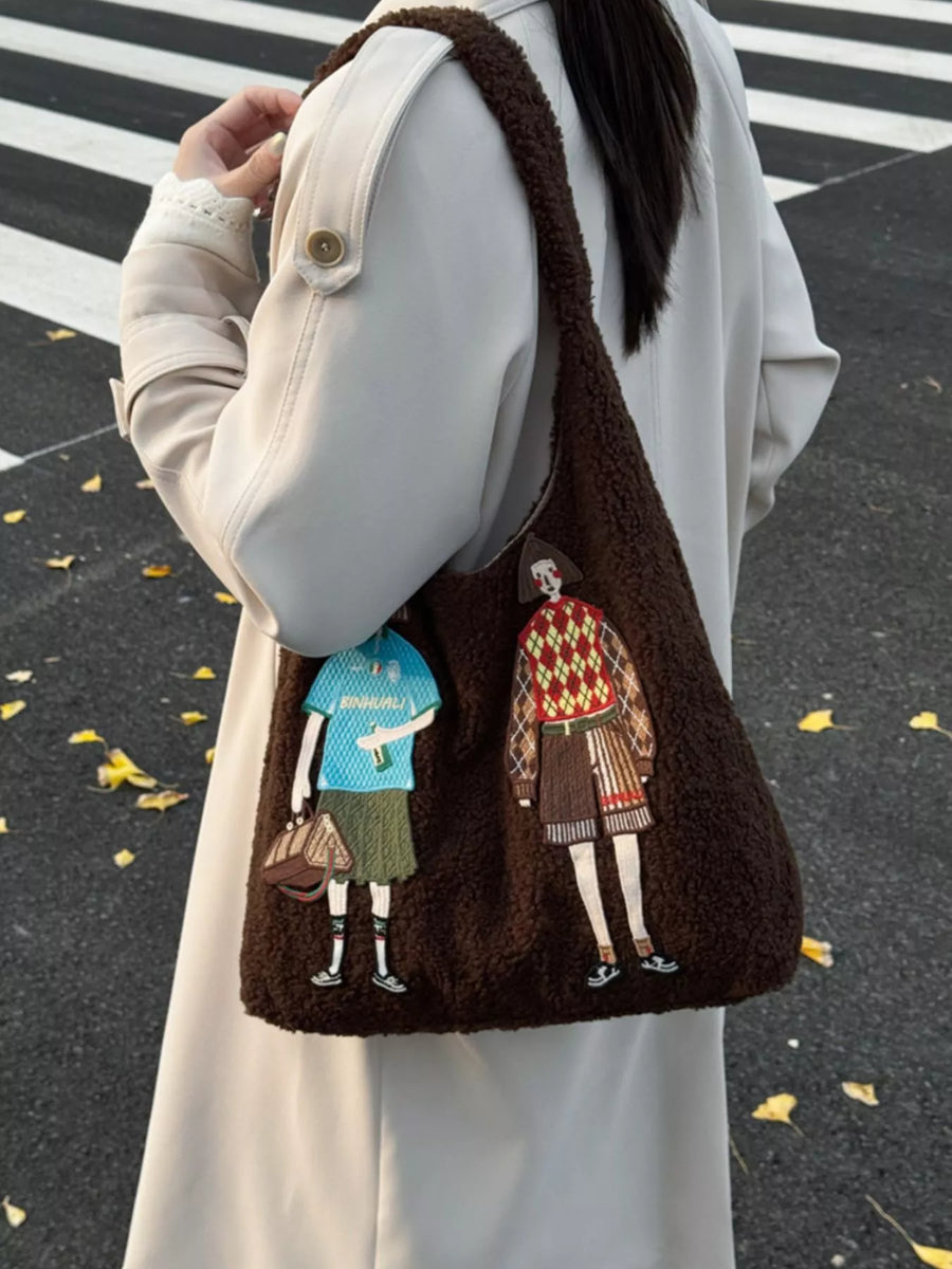 Brown textured bag with embroidered characters held by a person on a black and white striped background.