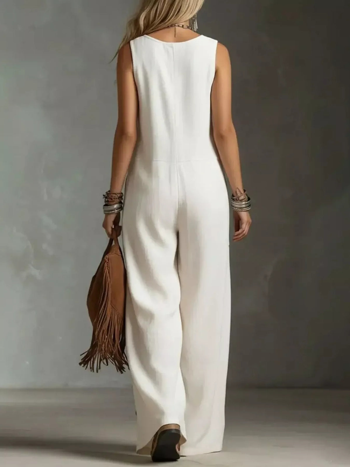 Person wearing a white sleeveless jumpsuit holding a brown leather bag against a neutral background