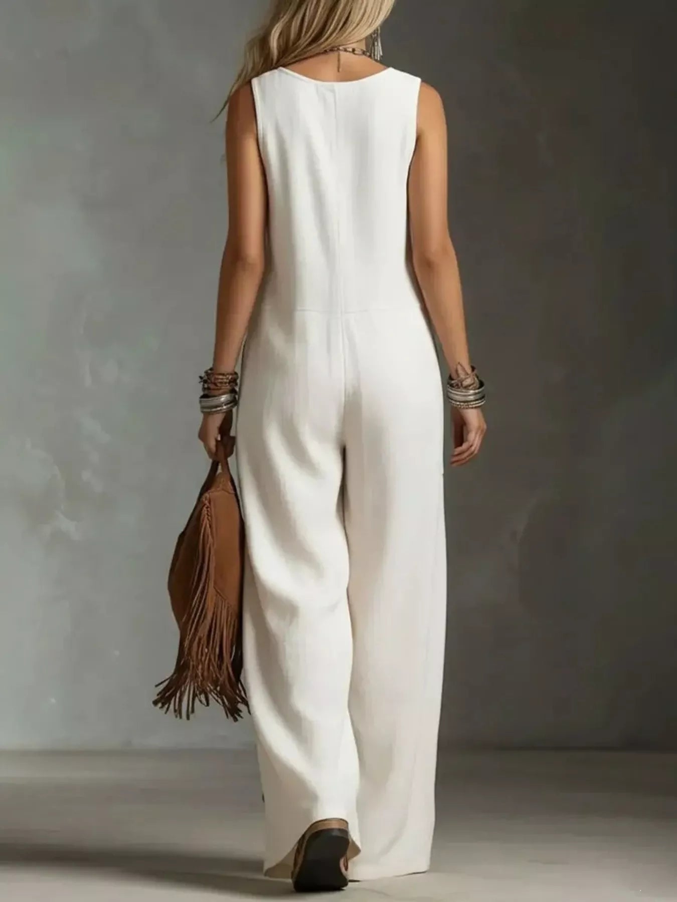 Person wearing a white sleeveless jumpsuit holding a brown leather bag against a neutral background