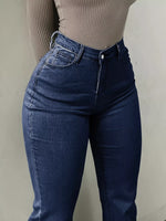 Person wearing blue jeans and a beige ribbed top against a plain background