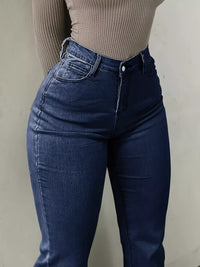 Person wearing blue jeans and a beige ribbed top against a plain background