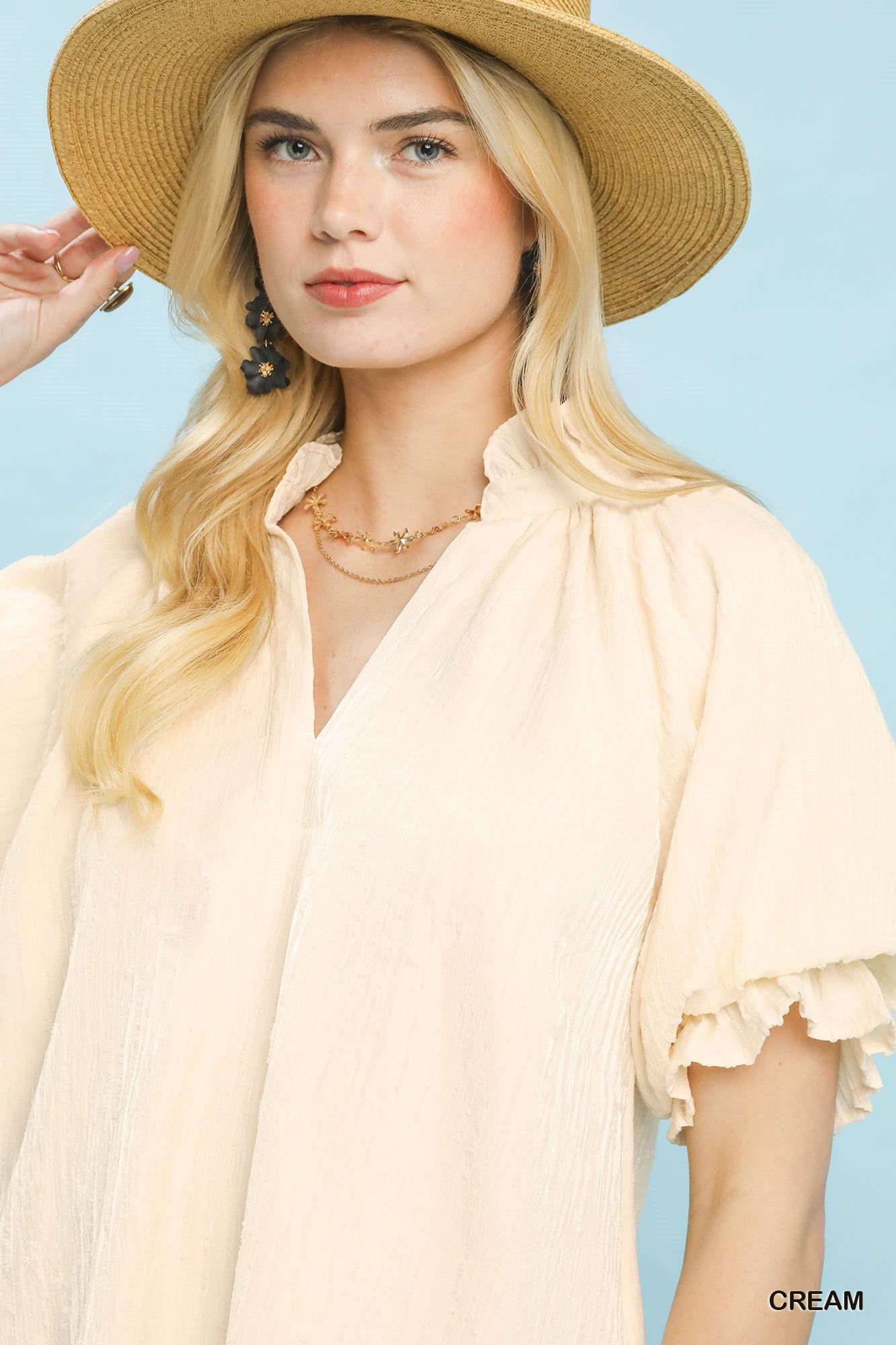 Woman wearing a cream blouse and straw hat against a light blue background