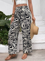 Person wearing black and white patterned pants with a white top and straw hat, standing on steps.