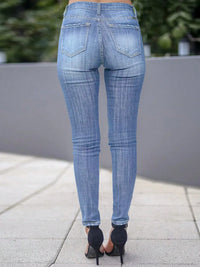 Person wearing blue jeans standing on a sidewalk with a blurred background