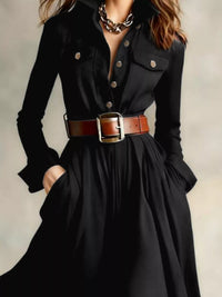 Black dress with a brown belt and chain necklace on a neutral background