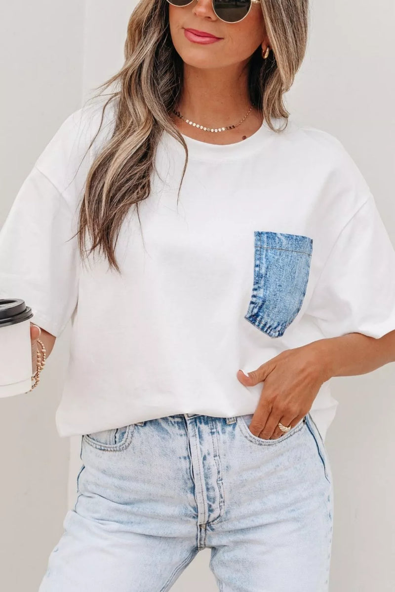 Person wearing a white t-shirt with a denim pocket and light blue jeans, holding a coffee cup.