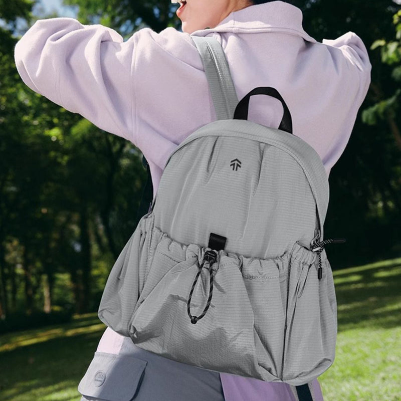Person wearing a gray backpack outdoors with greenery in the background