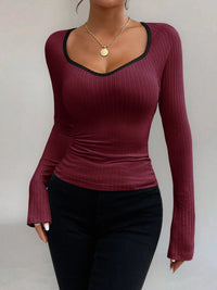 Person wearing a maroon long-sleeve top with black trim on a plain background