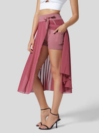 Woman wearing a pink wrap skirt over shorts on a plain background