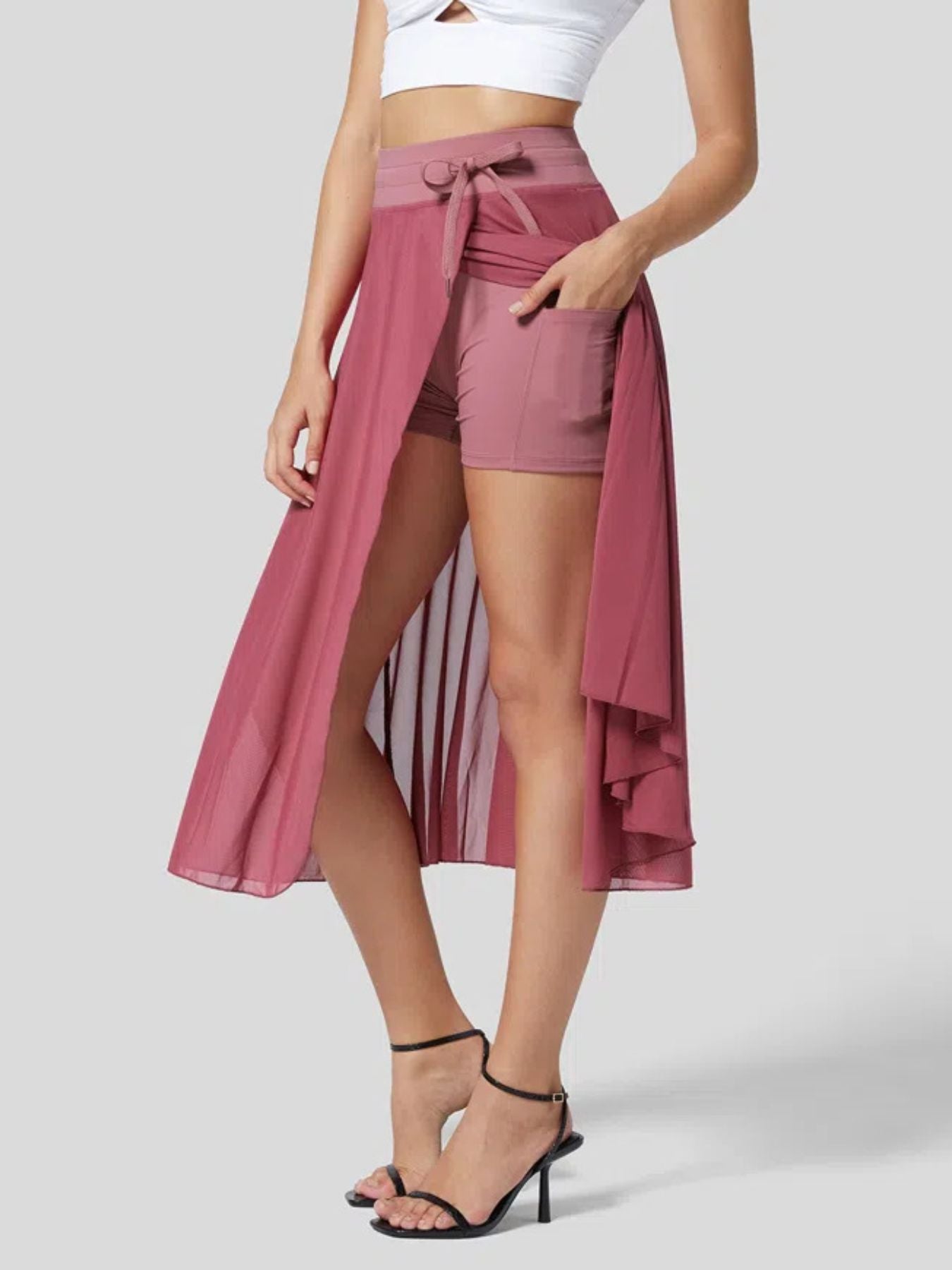 Woman wearing a pink wrap skirt over shorts on a plain background