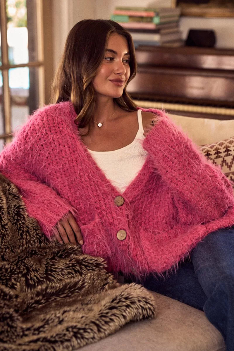 Woman wearing a pink cardigan sitting on a couch with a blurred background