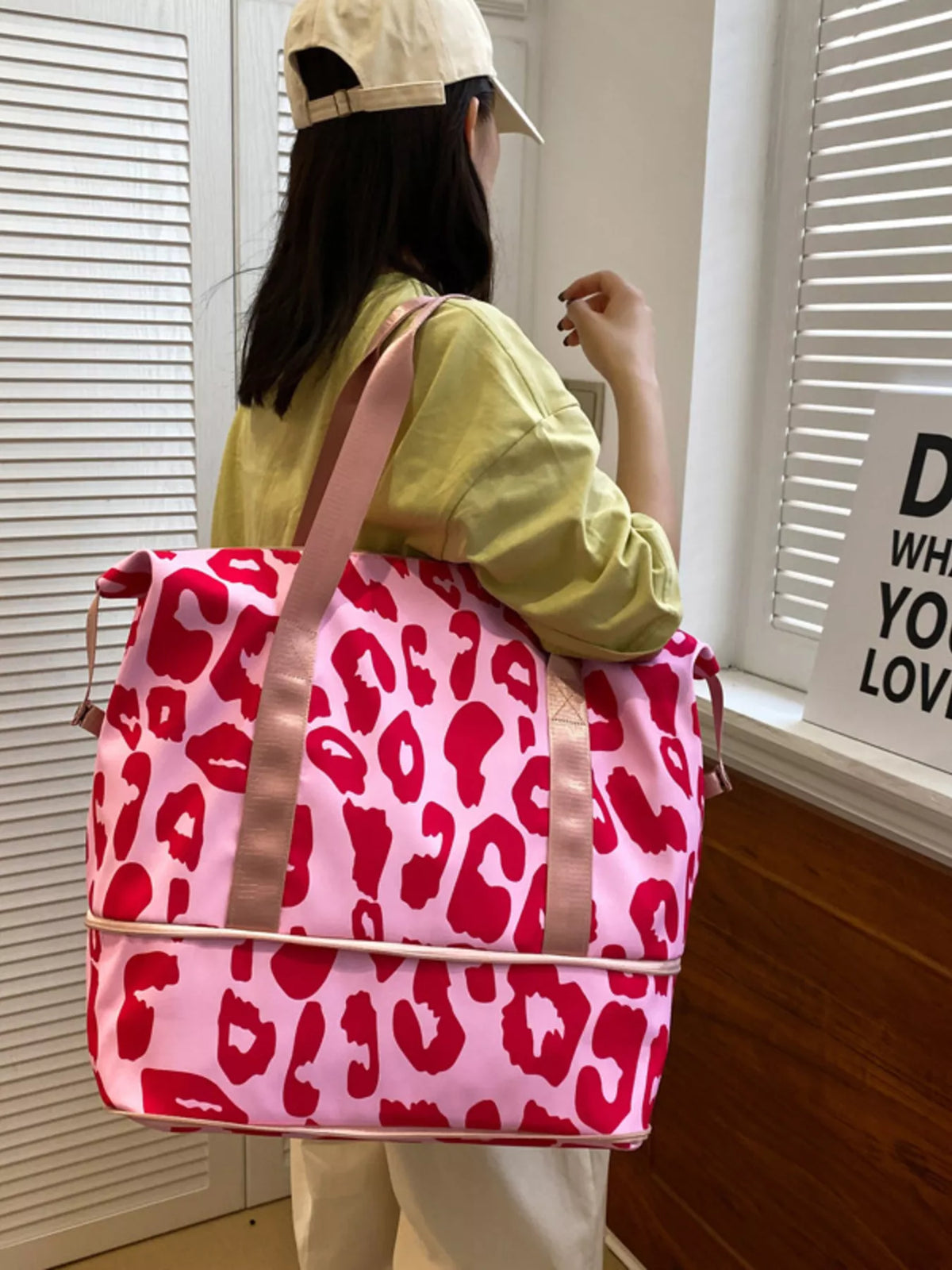 Person holding a pink backpack with red leopard print in a room.