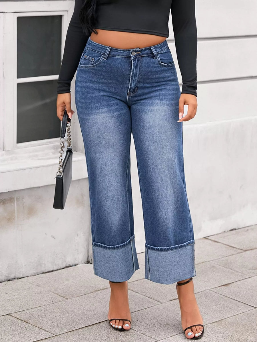 Person wearing blue wide-leg jeans and a black top against a light-colored wall.