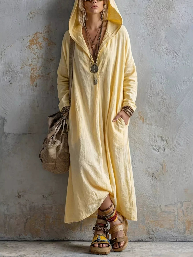 Woman wearing a long yellow dress with a hood against a textured wall.
