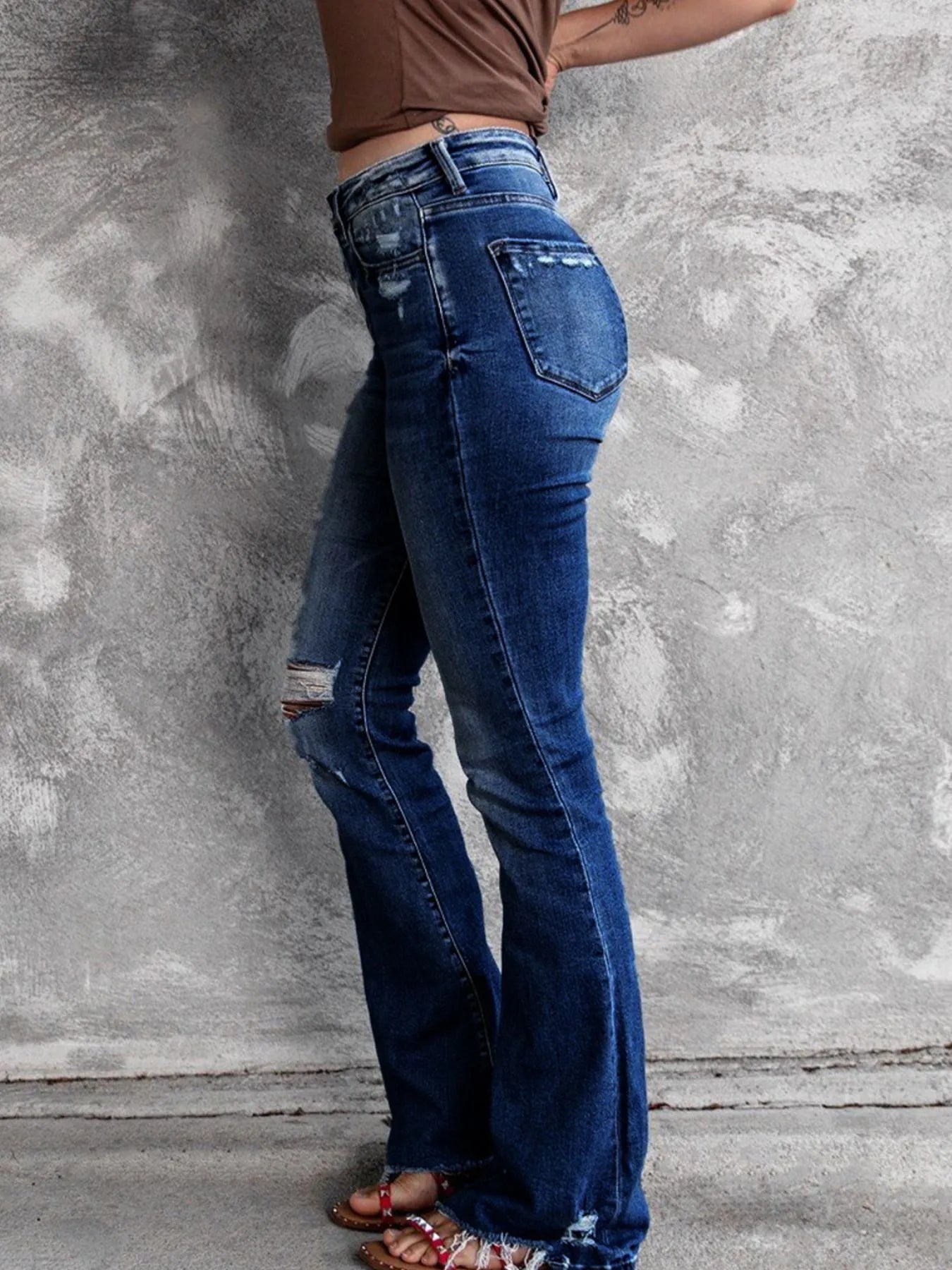 Person wearing blue flared jeans against a gray concrete wall.