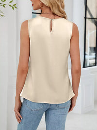 Woman wearing a beige sleeveless top and blue jeans indoors.