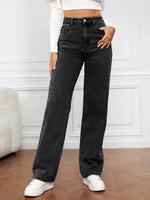 Person wearing black high-waisted jeans and white sneakers in a minimalistic room.