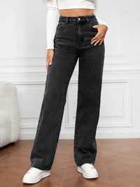 Person wearing black high-waisted jeans and white sneakers in a minimalistic room.