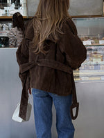 Person wearing a brown jacket and blue jeans standing in front of a display case.
