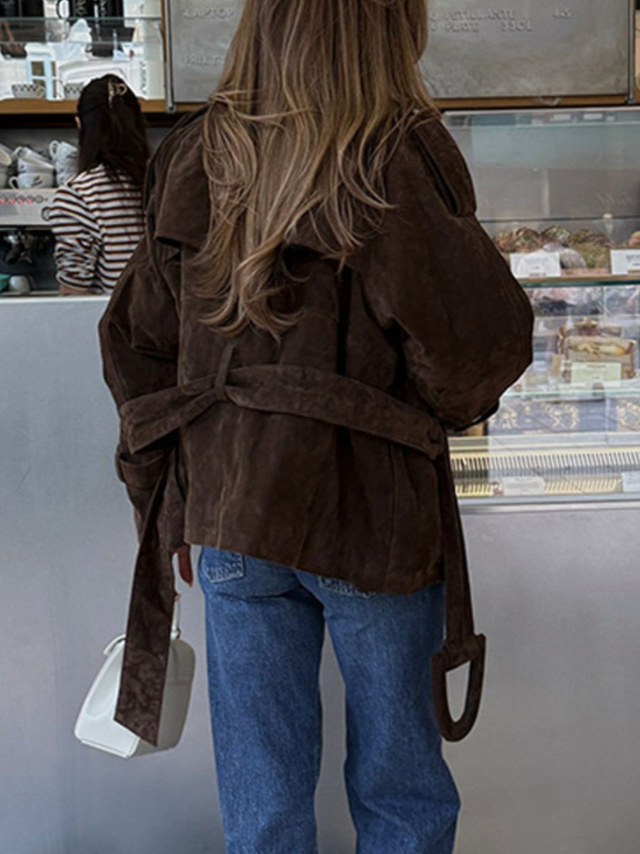 Person wearing a brown jacket and blue jeans standing in front of a display case.