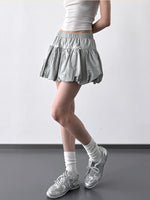 Person wearing a light gray skirt, white top, and white sneakers on a plain background