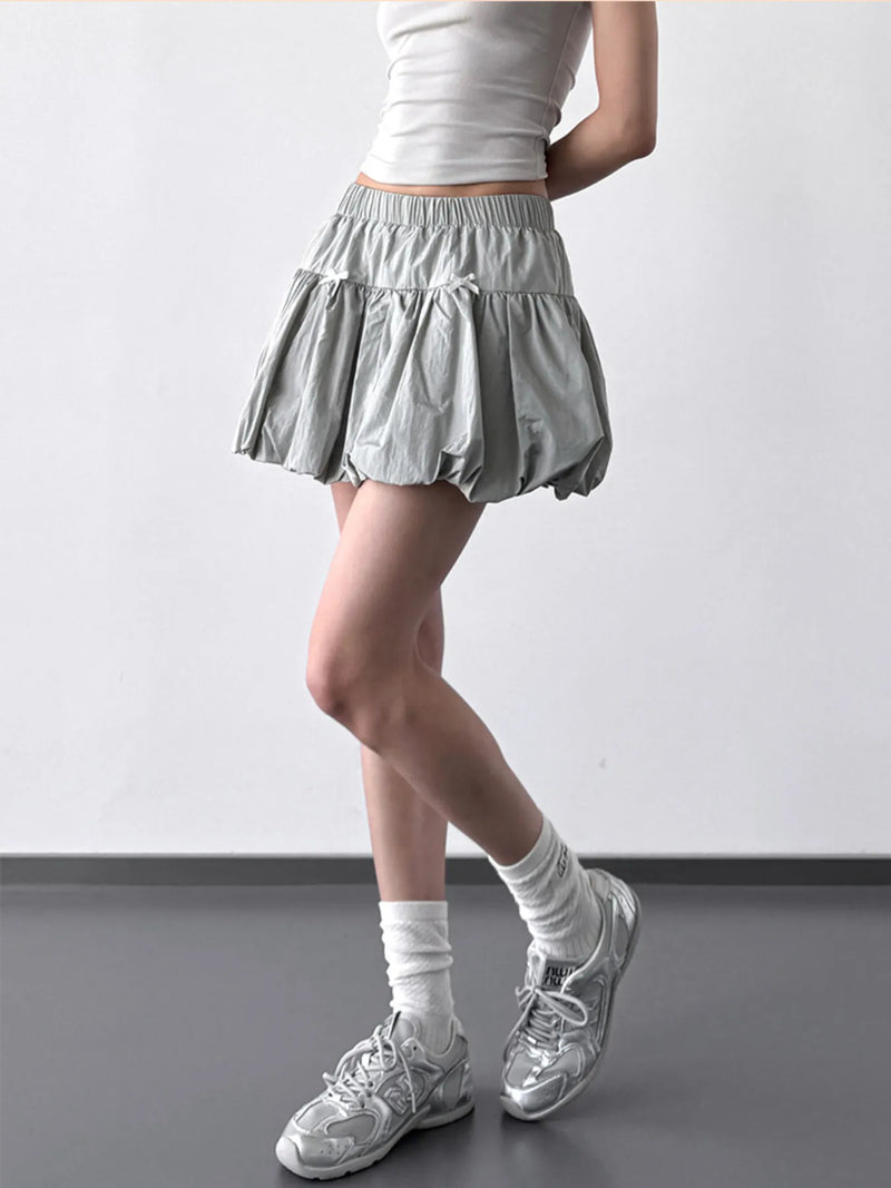 Person wearing a light gray skirt, white top, and white sneakers on a plain background