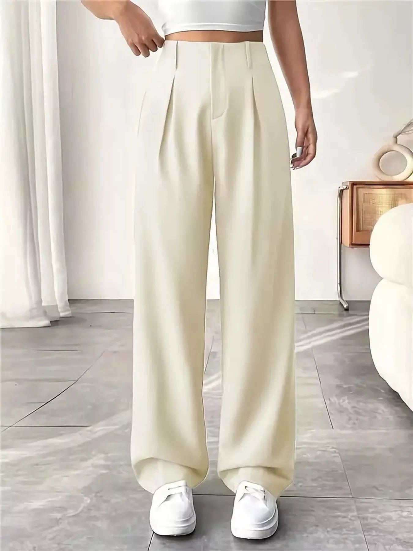 Person wearing cream-colored wide-leg pants and white sneakers in a minimalistic room.