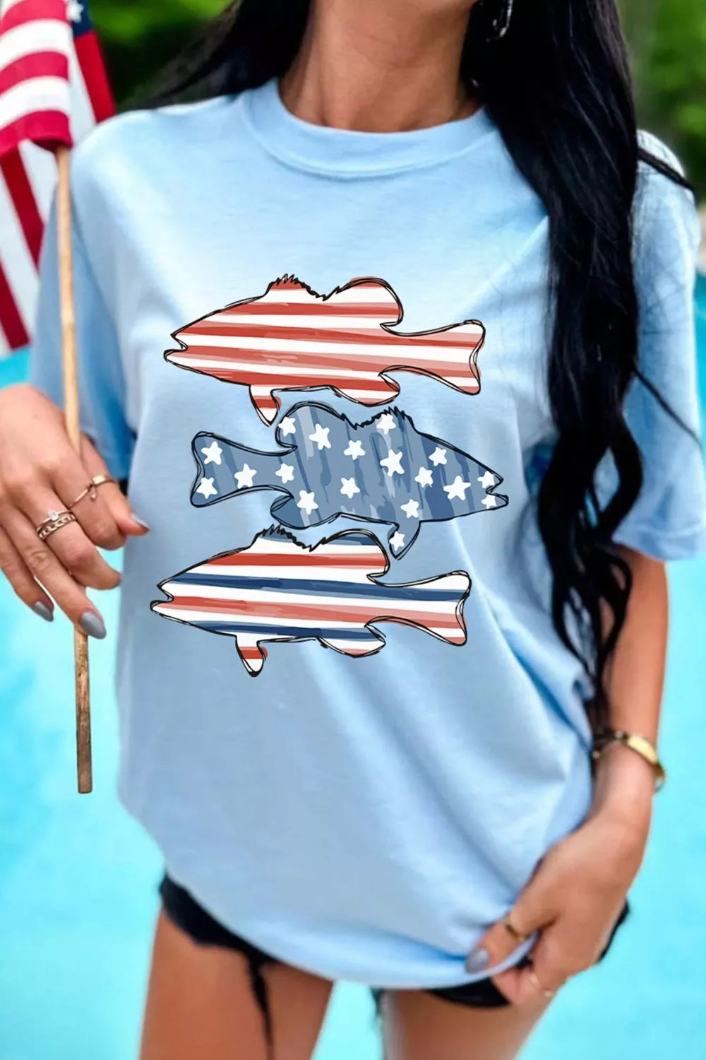 Woman wearing a light blue t-shirt with fish and American flag design, holding an American flag.