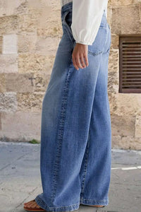 Person wearing wide-leg jeans with a stone wall background