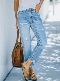 Person wearing light blue jeans with a brown bag and sandals on a blurred background