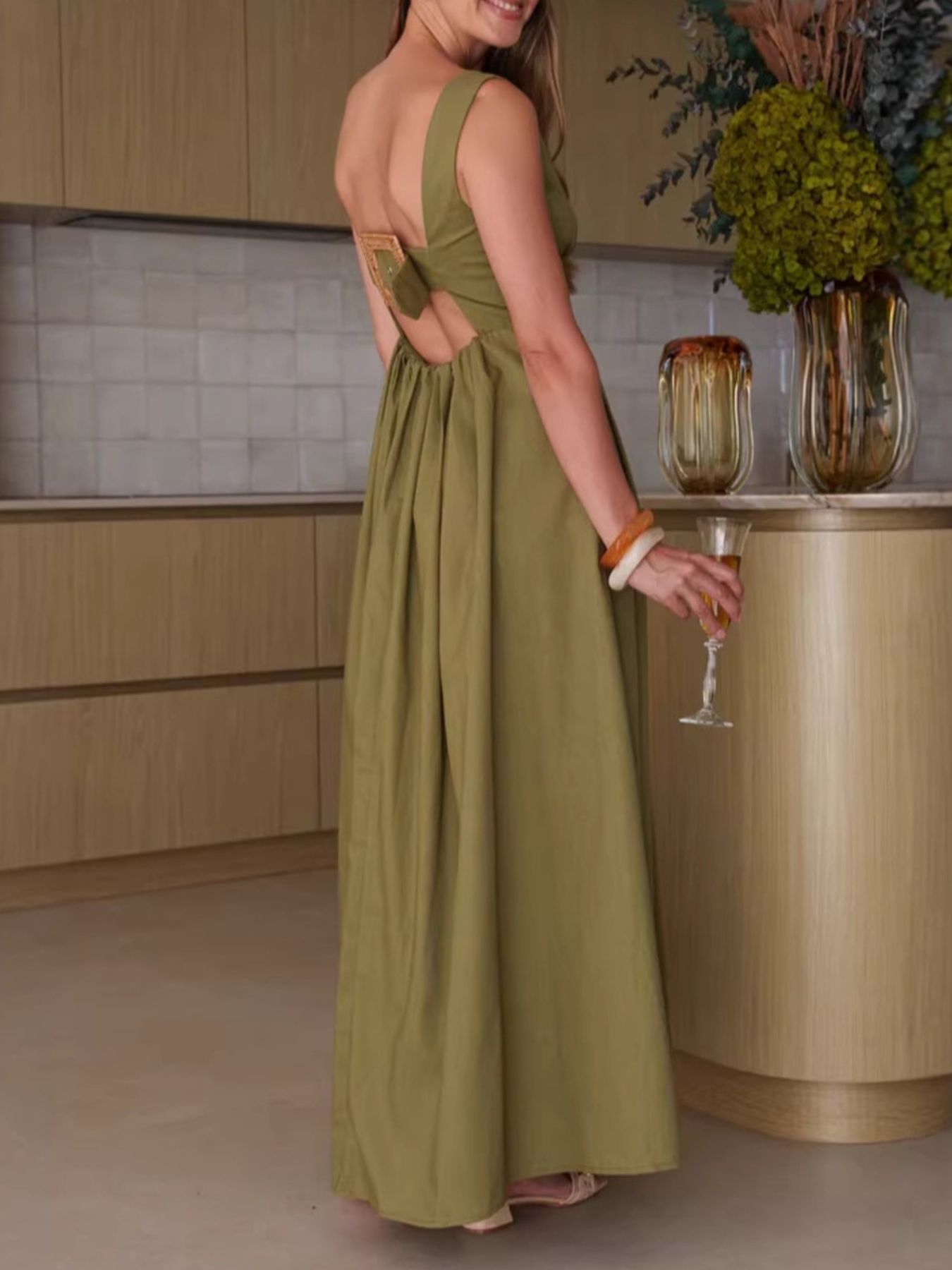Woman in a green dress holding a glass in a kitchen setting