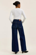 Person wearing blue jeans and a white long-sleeve shirt on a beige background