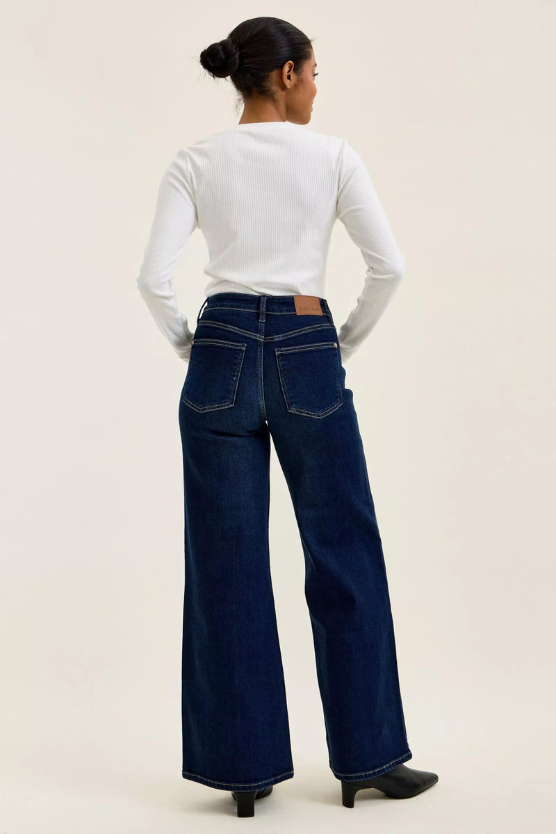 Person wearing blue jeans and a white long-sleeve shirt on a beige background