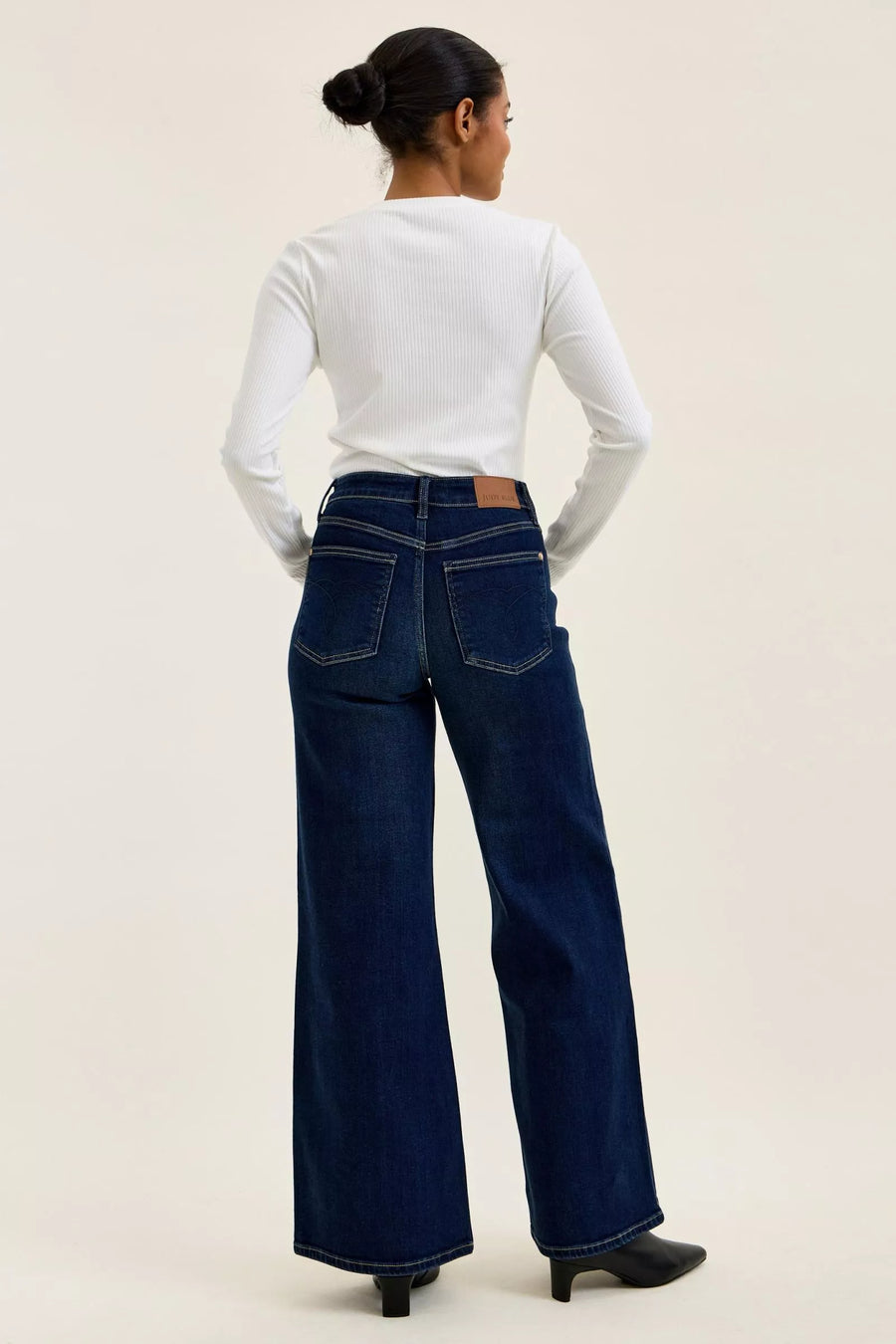 Person wearing blue jeans and a white long-sleeve shirt on a beige background
