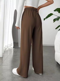 Brown wide-leg pants worn by a person in a minimalistic room.